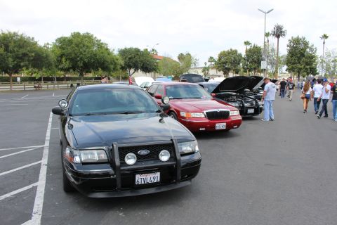 2003 Ford Crown Victoria - black Ford sedan with a brush guard leads a row of parked cars including a red sedan at an outdoor meet.