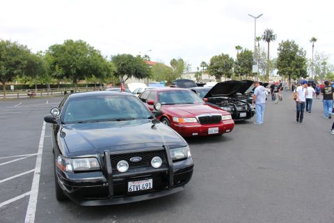 2003 Ford Crown Victoria - front of a black Ford sedan with a brush guard sits beside a red sedan in a row at a car show.