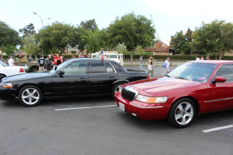 2003 Ford Crown Victoria - black sedan and a red Mercury sedan are parked close together near a street at a daytime car meet.