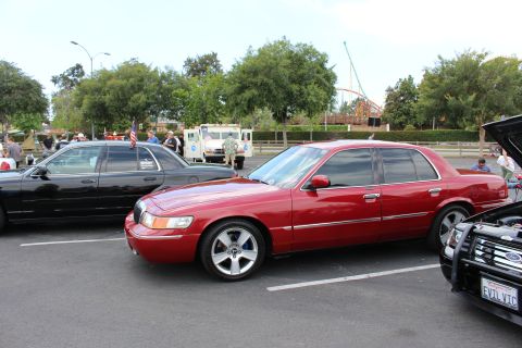 2003 Ford Crown Victoria - red Mercury Grand Marquis sedan on alloy wheels is parked at an outdoor car show with a coaster behind.