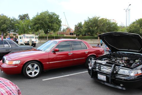 2003 Ford Crown Victoria - red Mercury sedan is parked beside a black Ford sedan with its hood open at an outdoor car meet.
