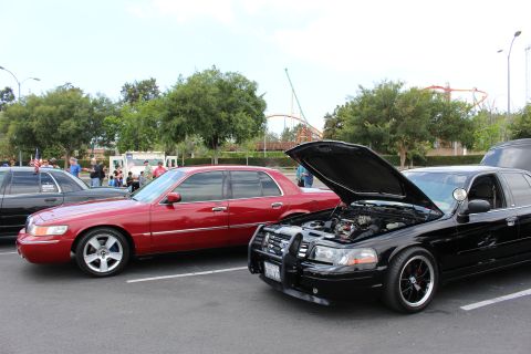 2003 Ford Crown Victoria - red Mercury sedan and a black sedan with raised hood sit side by side at a parking-lot car show.