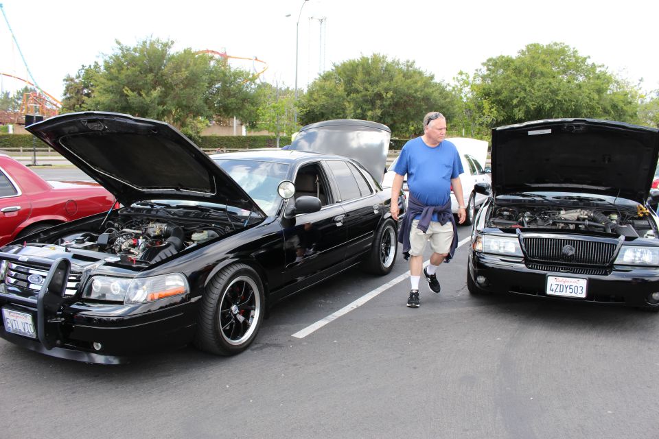 Man walks between two black sedans with hoods up at parking-lot car show