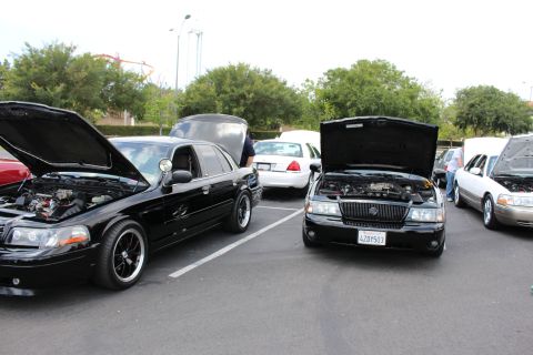 Two black Mercury sedans with hoods open parked at outdoor car meet