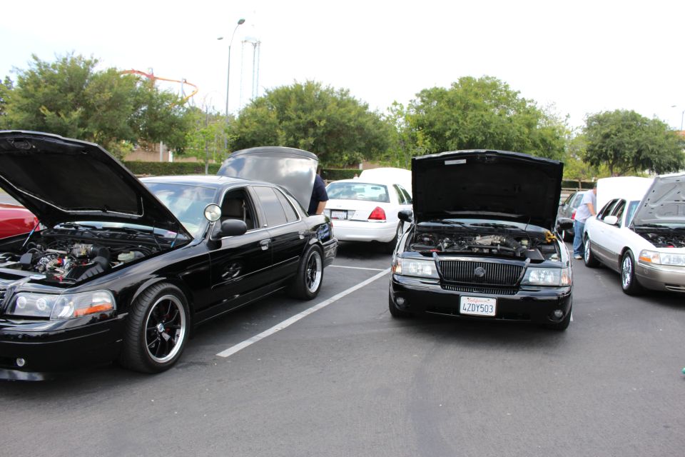 Two black Mercury sedans with hoods open parked at outdoor car meet