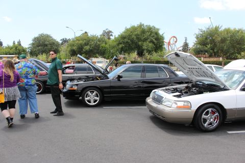 Black sedan with hood up and silver-gold Grand Marquis at a car show