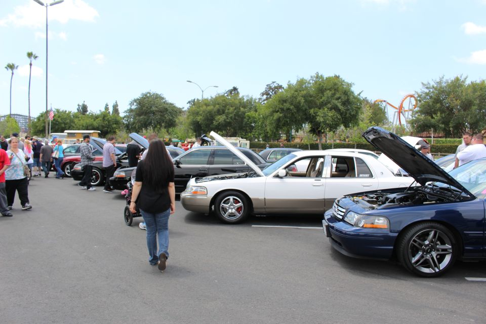 Row of sedans with hoods up and a crowd walking through a car show lot