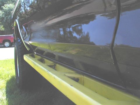 1979 Ford Bronco - Side view of a black SUV with yellow running boards, parked near a red truck.