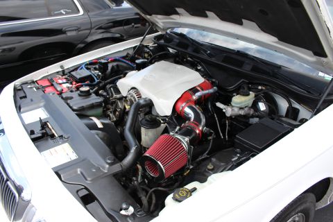 Engine bay of a white sedan with a red cone air intake and chrome plenum