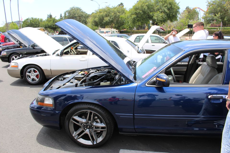 Blue Ford sedan with hood open beside a silver car at an outdoor car show