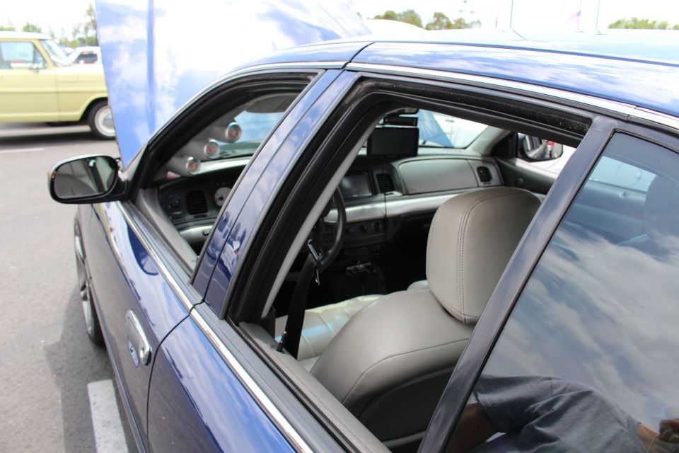 Open window of a blue sedan showing gray leather front seats and dashboard with A-pillar gauges