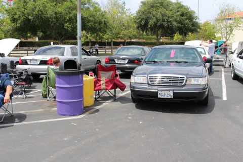 Gray Ford Crown Victoria with California license plate parked at a car show near chairs and a purple barrel