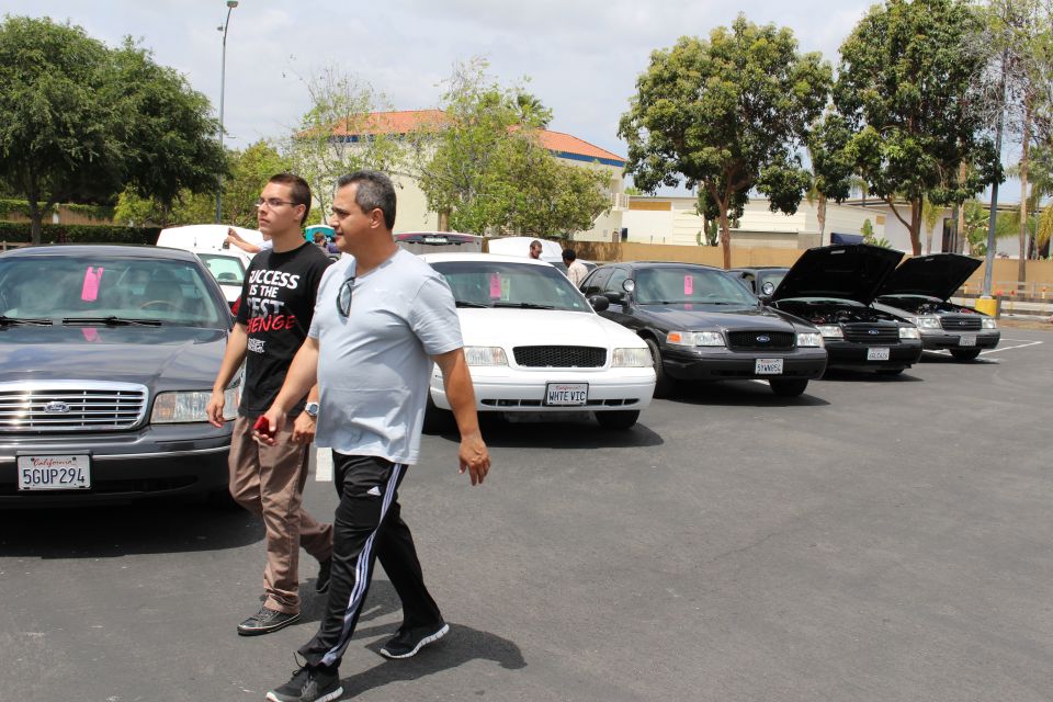 Two men walking past a row of Ford Crown Victoria sedans at an outdoor car show