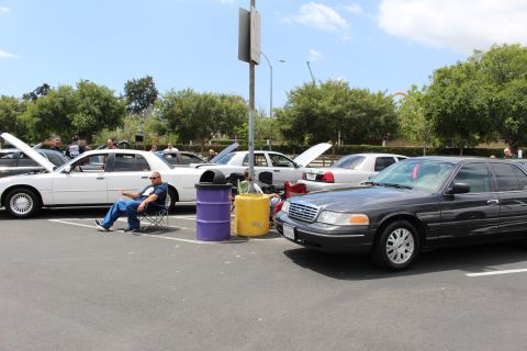 White Mercury Grand Marquis and a gray Ford Crown Victoria parked at a car show with a seated man