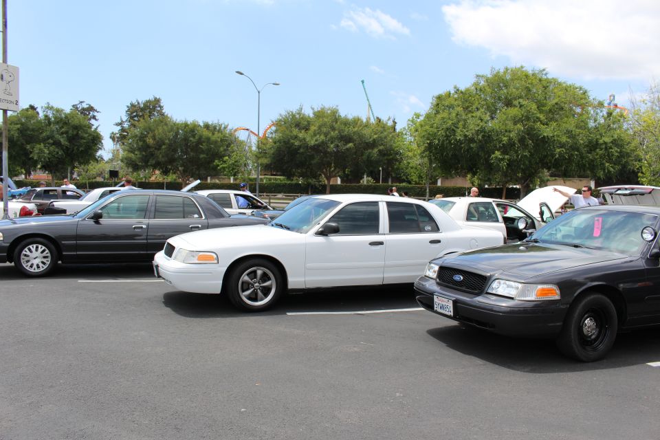 White Ford Crown Victoria between a gray and a black Crown Victoria in a car-show row