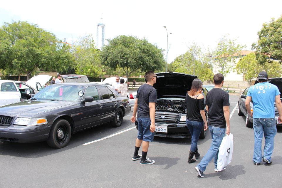 Black Ford Crown Victorias, one with hood up, with several people gathered at a car show