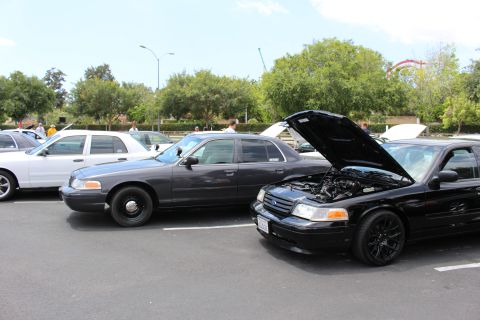Black Ford Crown Victoria with hood up and black wheels beside a dark and a white Crown Victoria