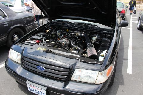 Engine bay of a black Ford sedan with cold-air intake at a car meet