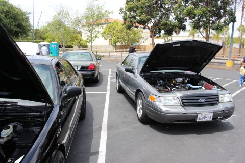 Gray Ford sedan with hood open parked next to a black sedan at a car show