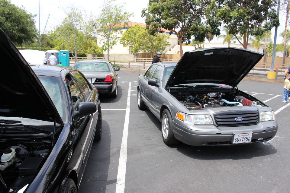 Gray Ford sedan with hood open parked next to a black sedan at a car show
