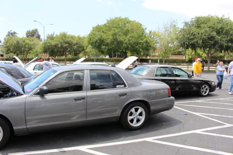 Gray and black full-size sedans parked in a lot with people nearby