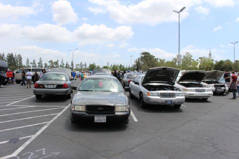 Row of sedans including a silver Lincoln with hood up at car meet