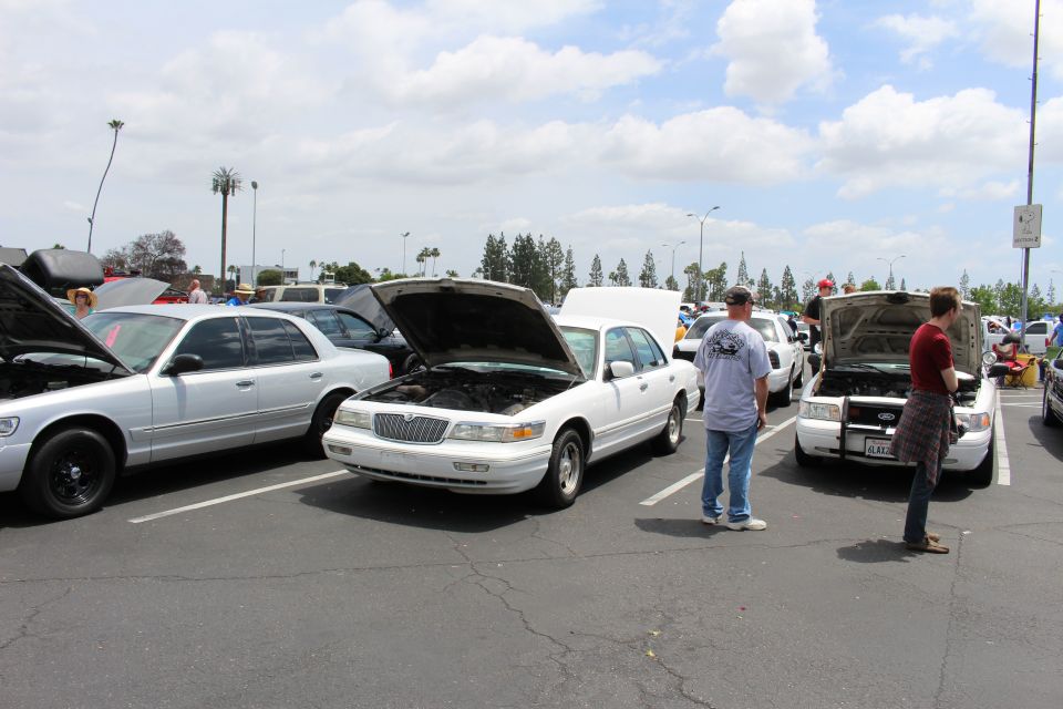White full-size sedan with hood up parked beside a silver sedan at an outdoor car meet