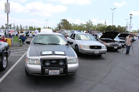 Silver Ford sedan with push bar and HELLA lights facing camera among parked cars