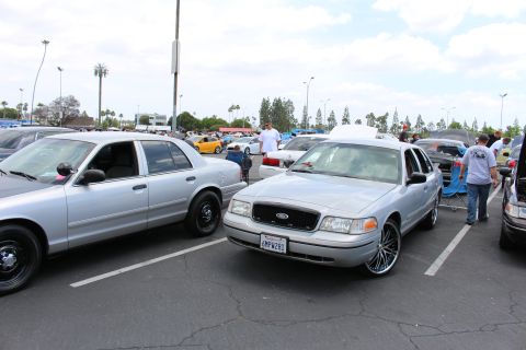 Silver Ford sedan on chrome multi-spoke wheels beside another silver sedan at a meet