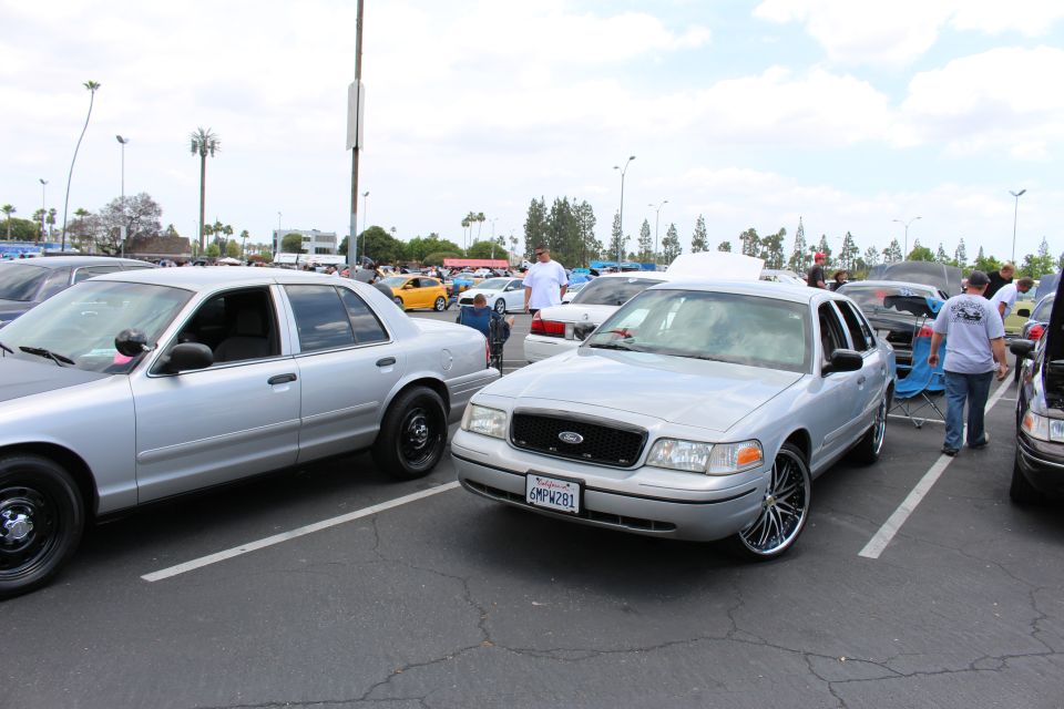 Silver Ford sedan on chrome multi-spoke wheels beside another silver sedan at a meet