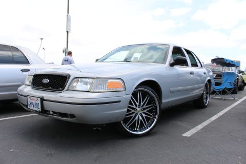 Silver Ford sedan on large black-and-chrome wheels parked at an outdoor car meet