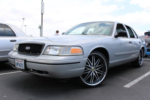 Front three-quarter of a silver Ford sedan on big black-and-chrome wheels at a meet