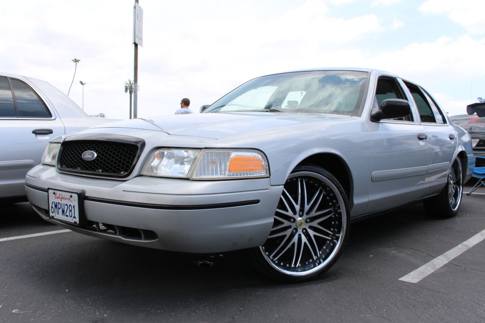 Front three-quarter of a silver Ford sedan on big black-and-chrome wheels at a meet