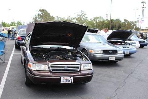 Maroon Ford sedan with open hood showing engine bay beside other sedans at a meet