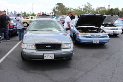 Gray Ford sedan with CHP P71 plate beside a blue car with open hood at a car meet