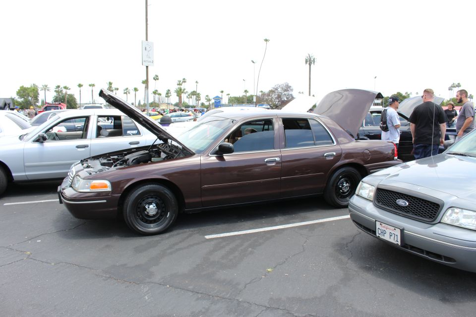 Brown Ford Crown Victoria sedan with hood open at an outdoor car show parking lot