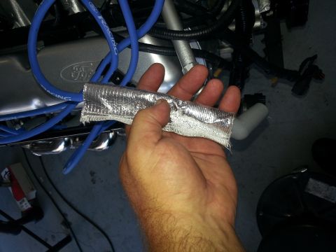 1994 Ford Bronco - Close-up of a hand holding a heat shield over spark plug wires on an engine.