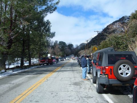 1988 Ford Bronco - Several vehicles are parked along a road with snow on the ground and mountains in the background.