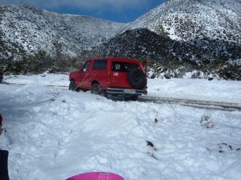1988 Ford Bronco - A red SUV navigates a snowy mountain road, with a spare tire mounted on the back.