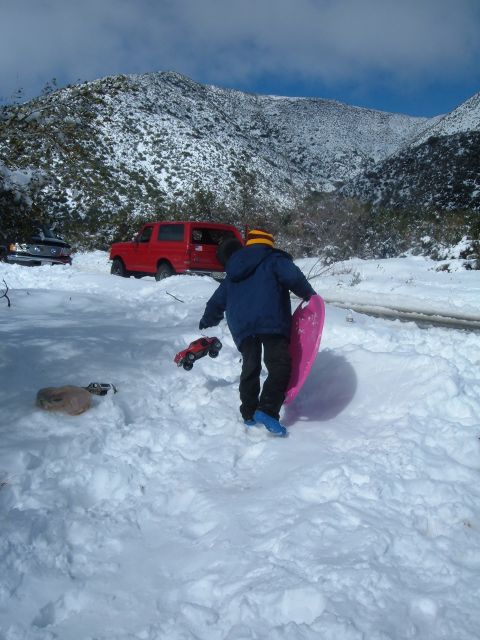 1988 Ford Bronco - A red SUV is parked in a snowy landscape, with a person in the foreground holding a pink sled and a toy car.