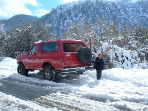 1988 Ford Bronco - A red Ford Bronco is parked in a snowy landscape with a child standing nearby.