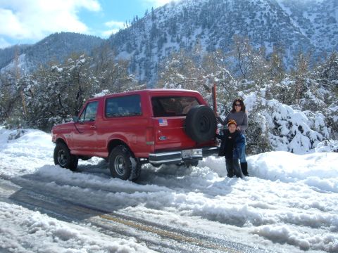 1988 Ford Bronco - A red 1988 Ford Bronco is parked on a snow-covered road with a woman and child nearby.