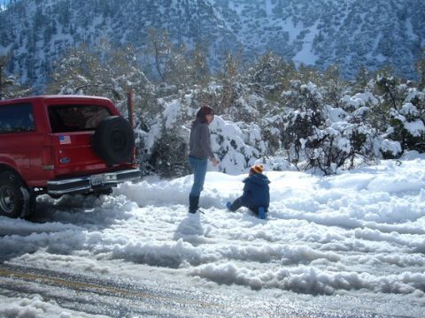 1988 Ford Bronco - A red SUV is parked in a snowy landscape with two people nearby.