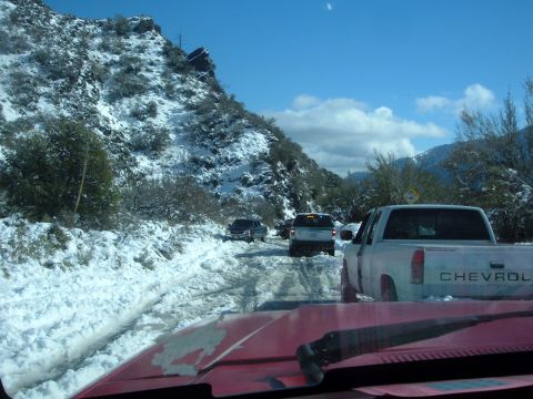1988 Ford Bronco - Vehicles are stuck in a snow-covered mountain pass, with a white Chevrolet pickup in the foreground.