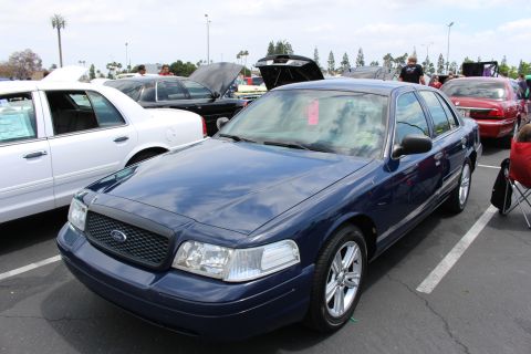 Dark blue Ford Crown Victoria sedan parked at a car show with people seated nearby