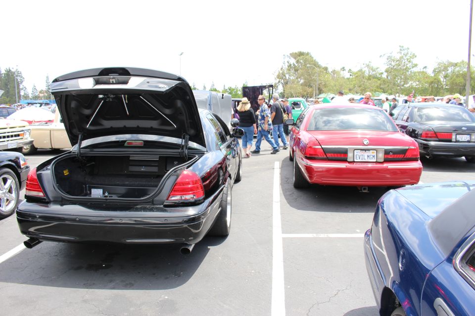 Black sedan with open trunk beside a red Grand Marquis at an outdoor car meet