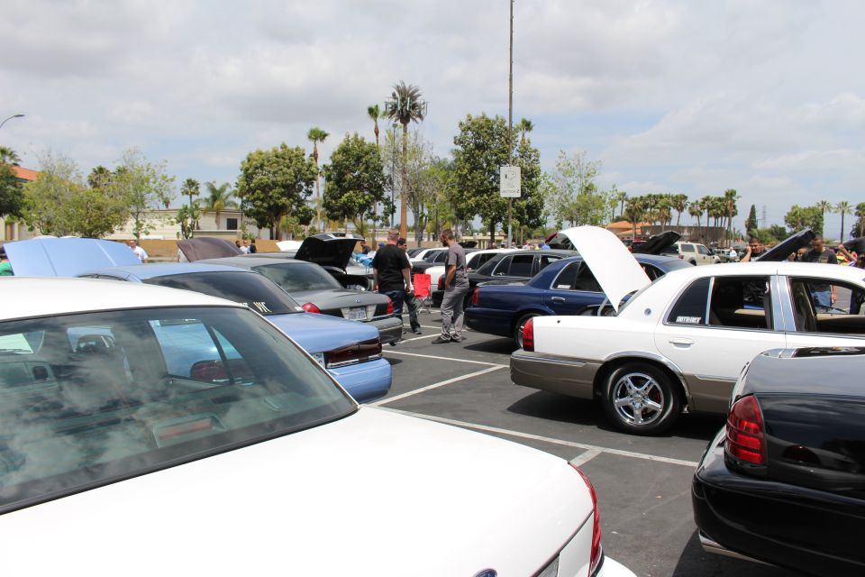 Crowded outdoor parking lot full of sedans with hoods up at a car show