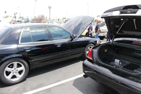 Black sedan with open hood beside a black sedan with open trunk at a car show