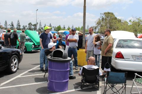 Group of people standing and talking by a purple trash barrel at a car show