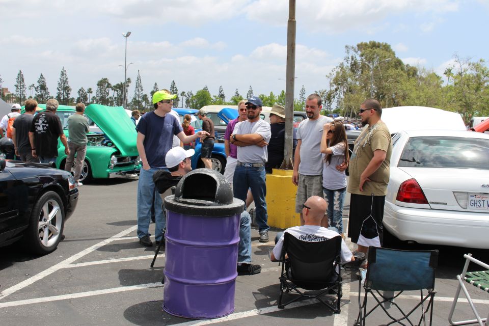 Group of people standing and talking by a purple trash barrel at a car show